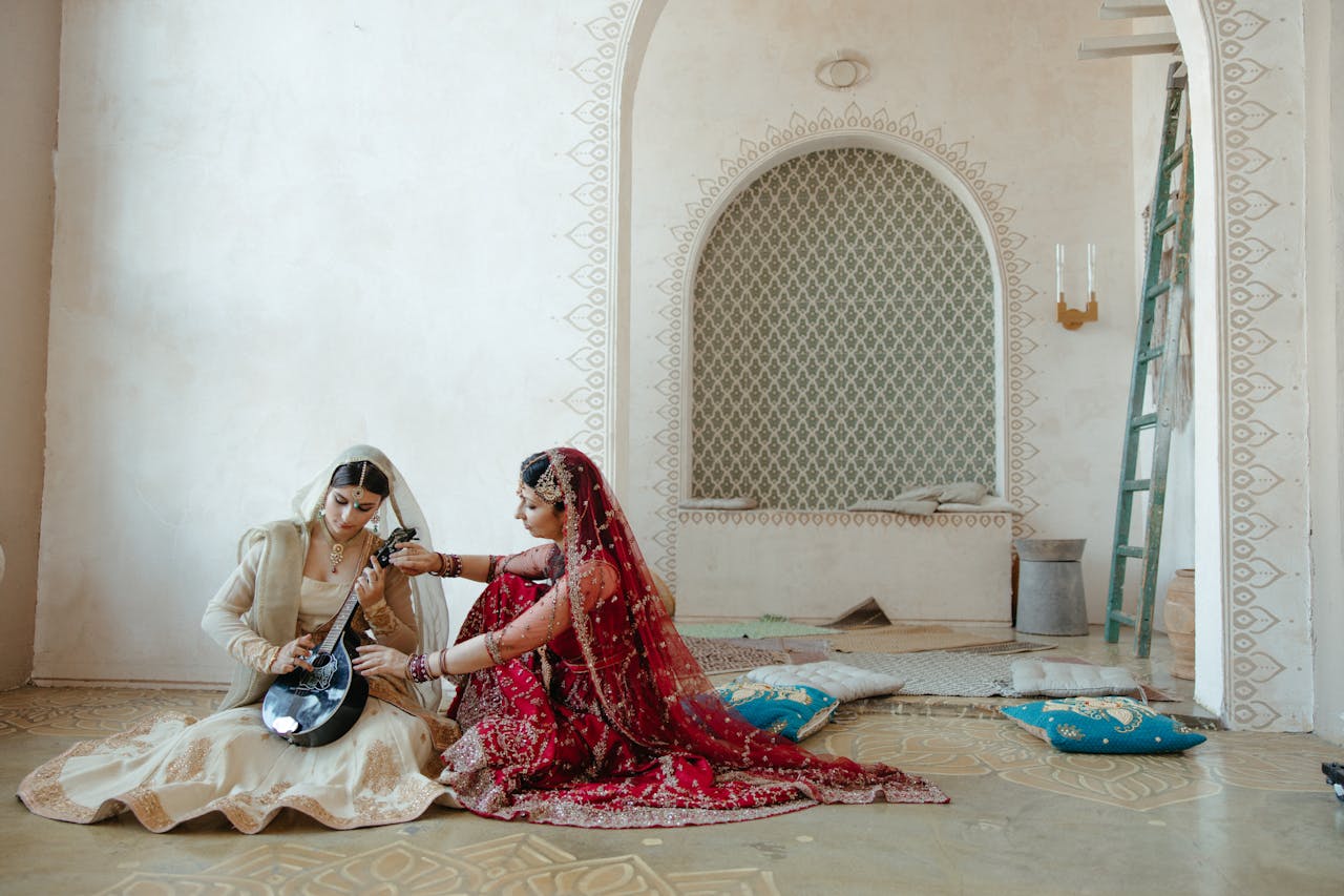 Two women in traditional Indian attire playing a stringed instrument indoors.